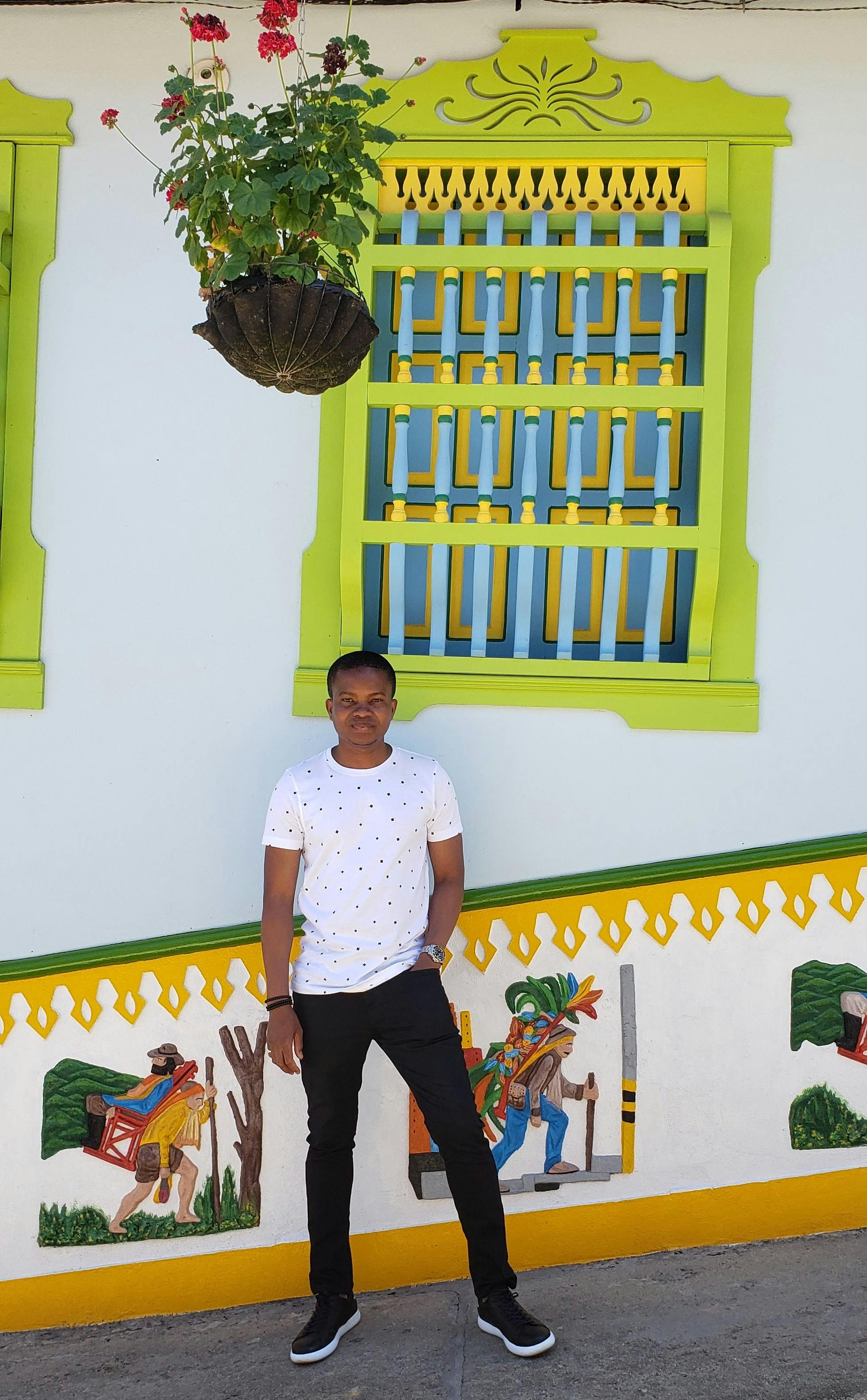 Young man in casual attire standing by vibrant wall in Guatapé, Colombia.