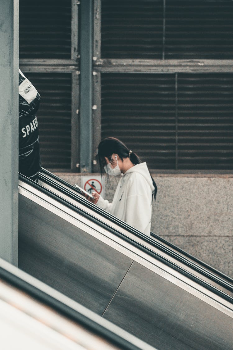 Masked Person With A Smartphone On An Escalator