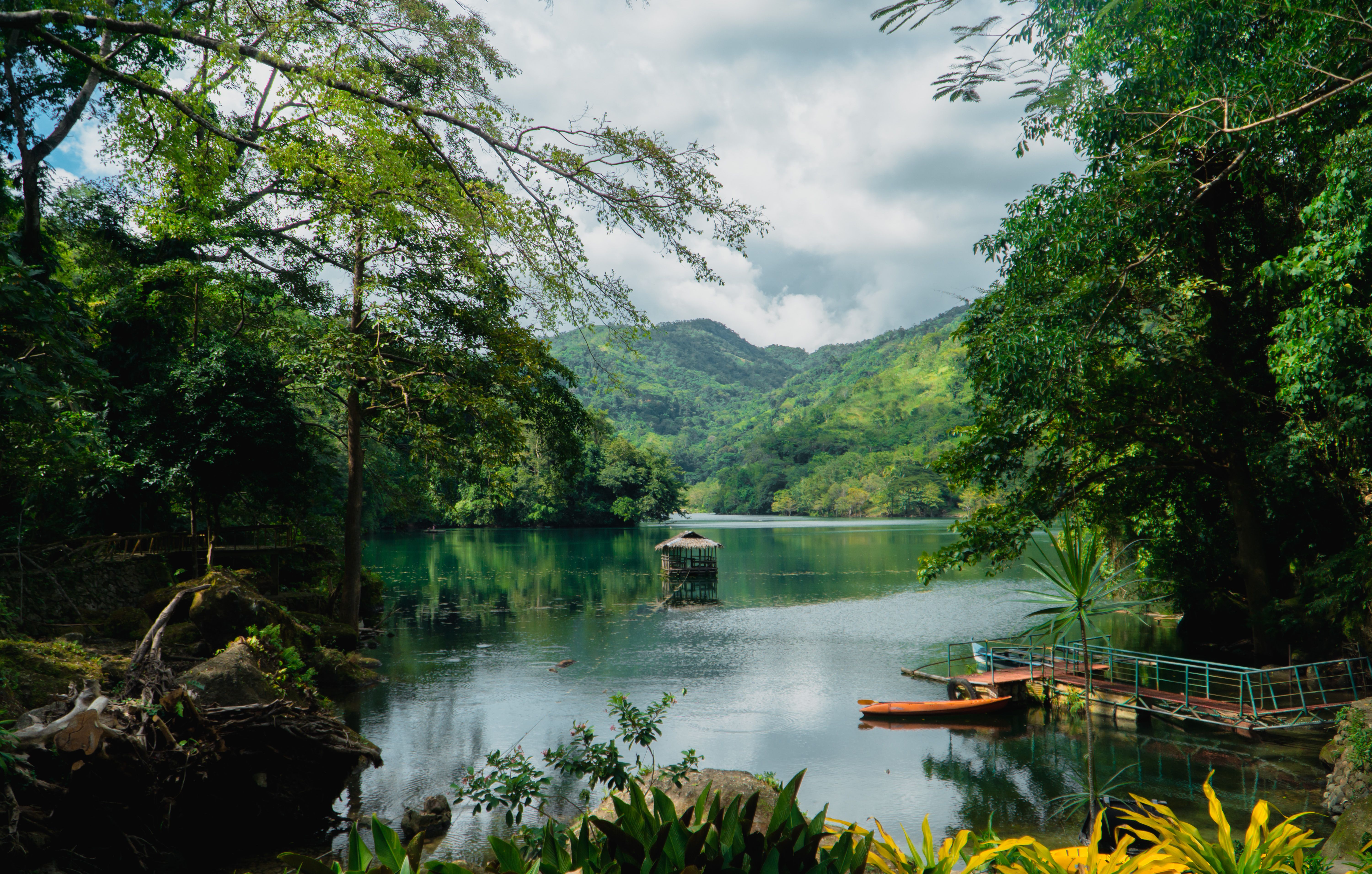 A tranquil lake surrounded by verdant trees and majestic mountains under a cloudy sky.