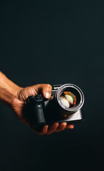 A close-up shot of a hand holding a camera against a black background.