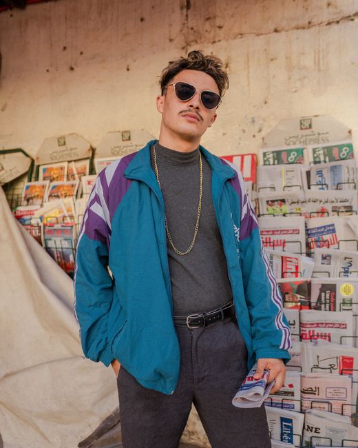 Vintage portrait of a man in a colorful jacket and sunglasses, standing in front of a magazine stand in Morocco.