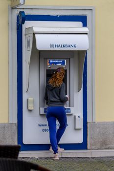 A woman uses an ATM machine outdoors on a city street during the day.