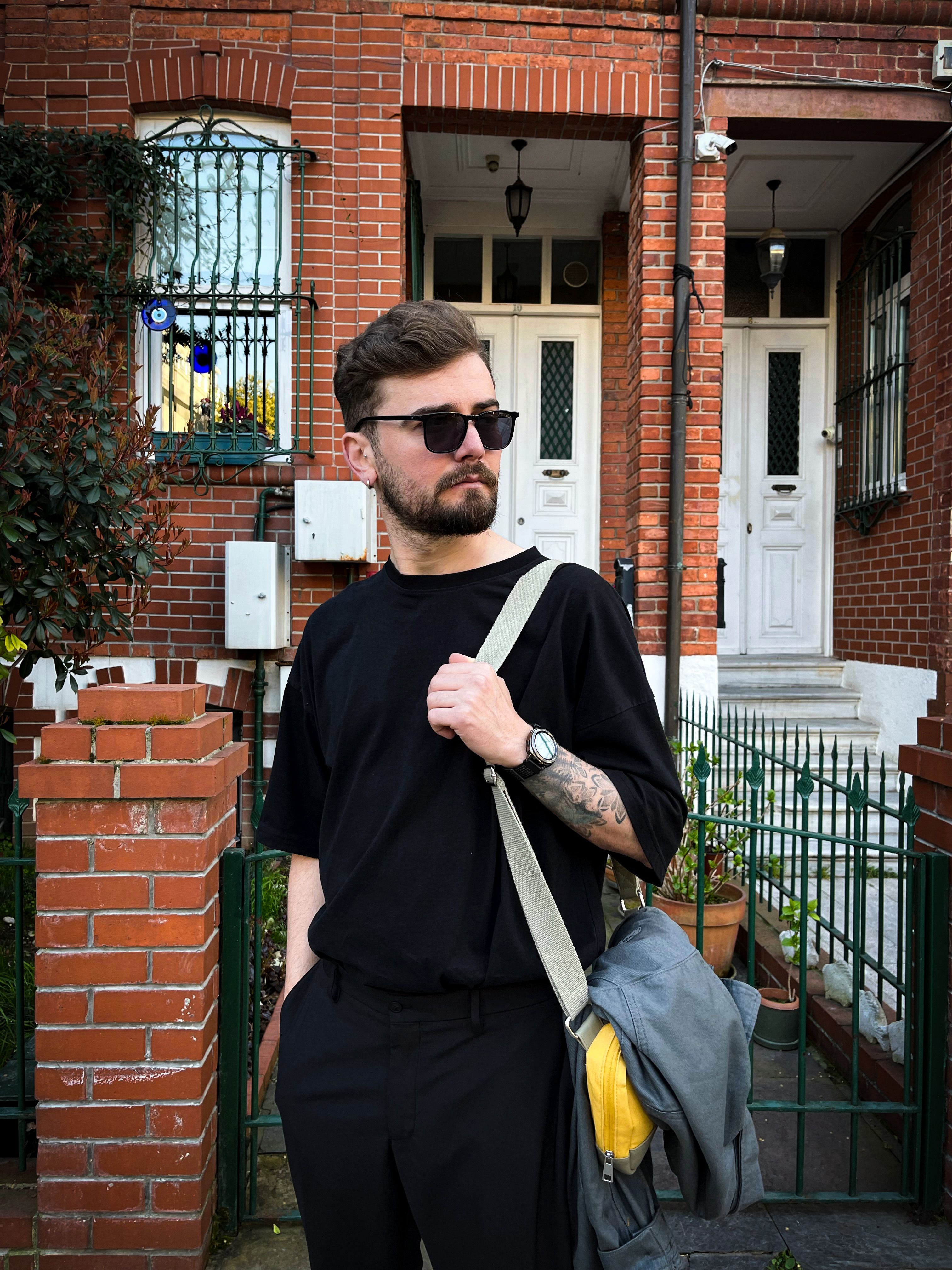 Casual fashion portrait of a man with sunglasses and backpack in front of city homes.