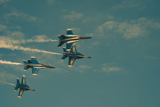 Four Navy jets perform a stunning aerial maneuver in a clear blue sky.