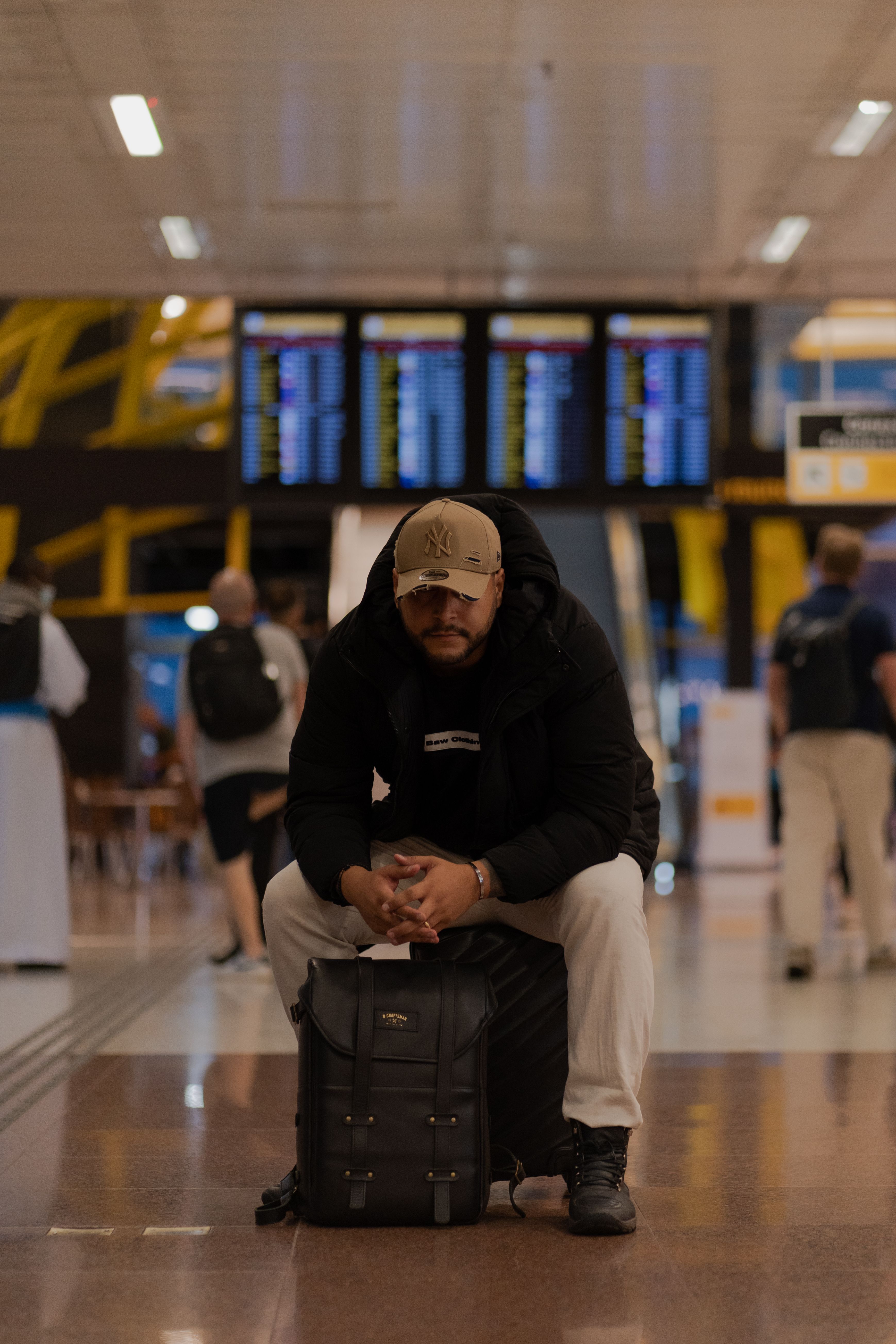 Free A traveler sitting on a suitcase in an airport terminal, surrounded by passengers. Stock Photo
