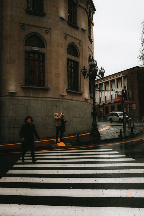 Free Rainy urban scene in Ankara, Türkiye with people crossing at a city crosswalk outside a historic building. Stock Photo