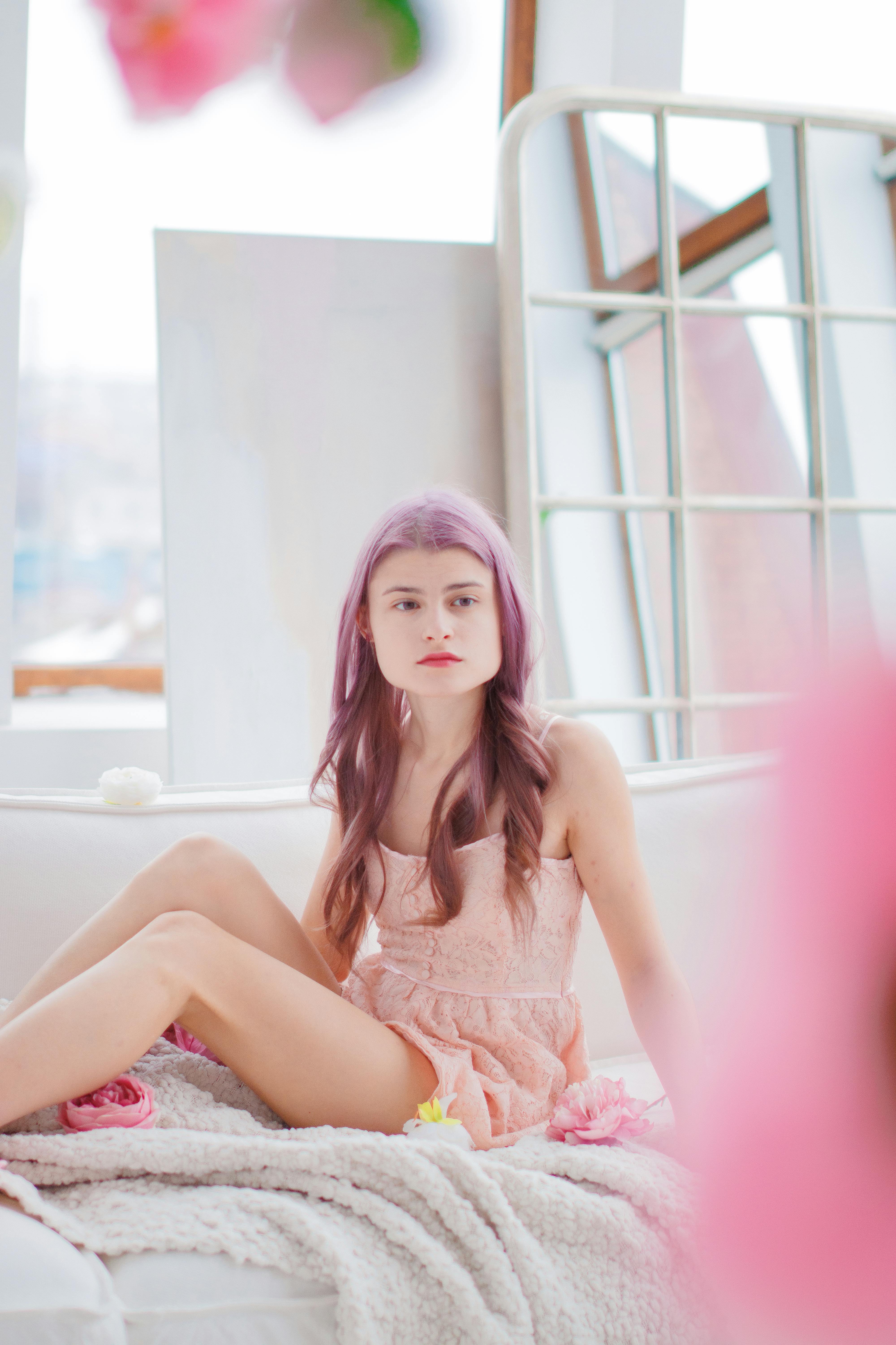 Portrait of a fashionable woman with pink hair sitting comfortably indoors in a modern setting.