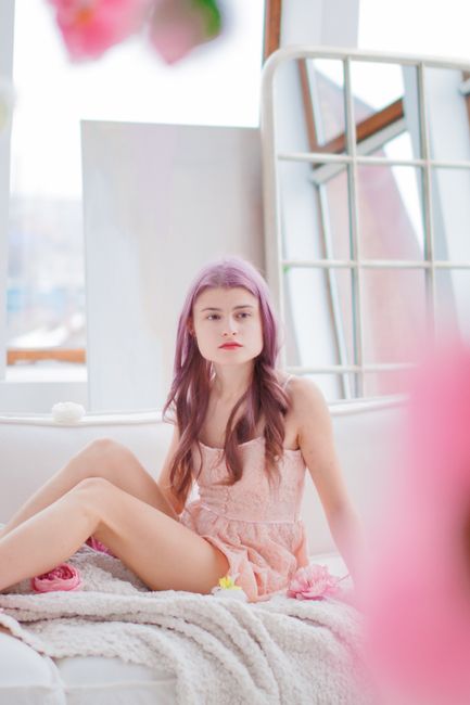 Portrait of a fashionable woman with pink hair sitting comfortably indoors in a modern setting.