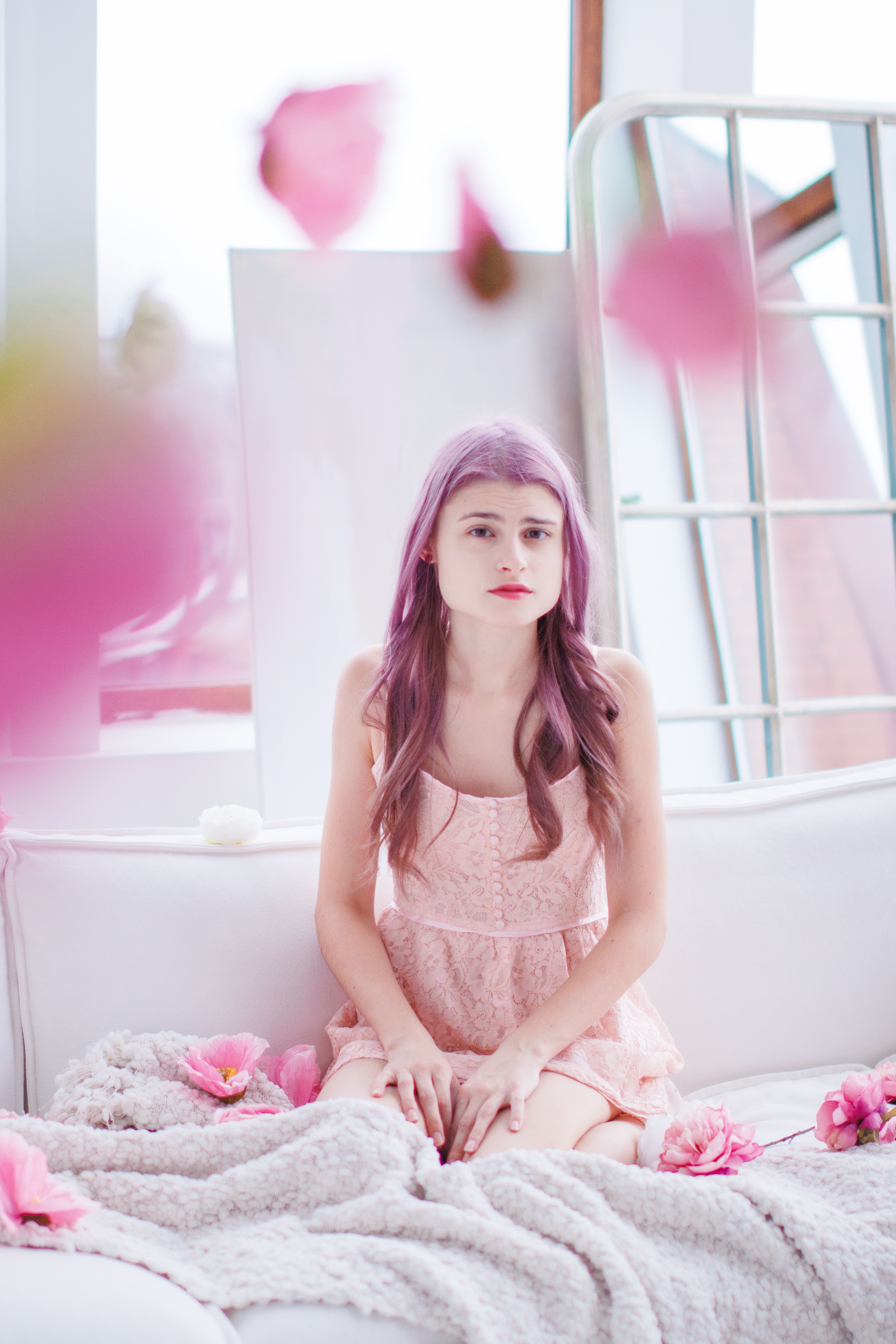 Young woman with pastel hair poses indoors surrounded by pink petals.