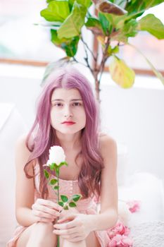 Beautiful portrait of a woman with pink hair holding a rose, captured in a soft, bright setting.