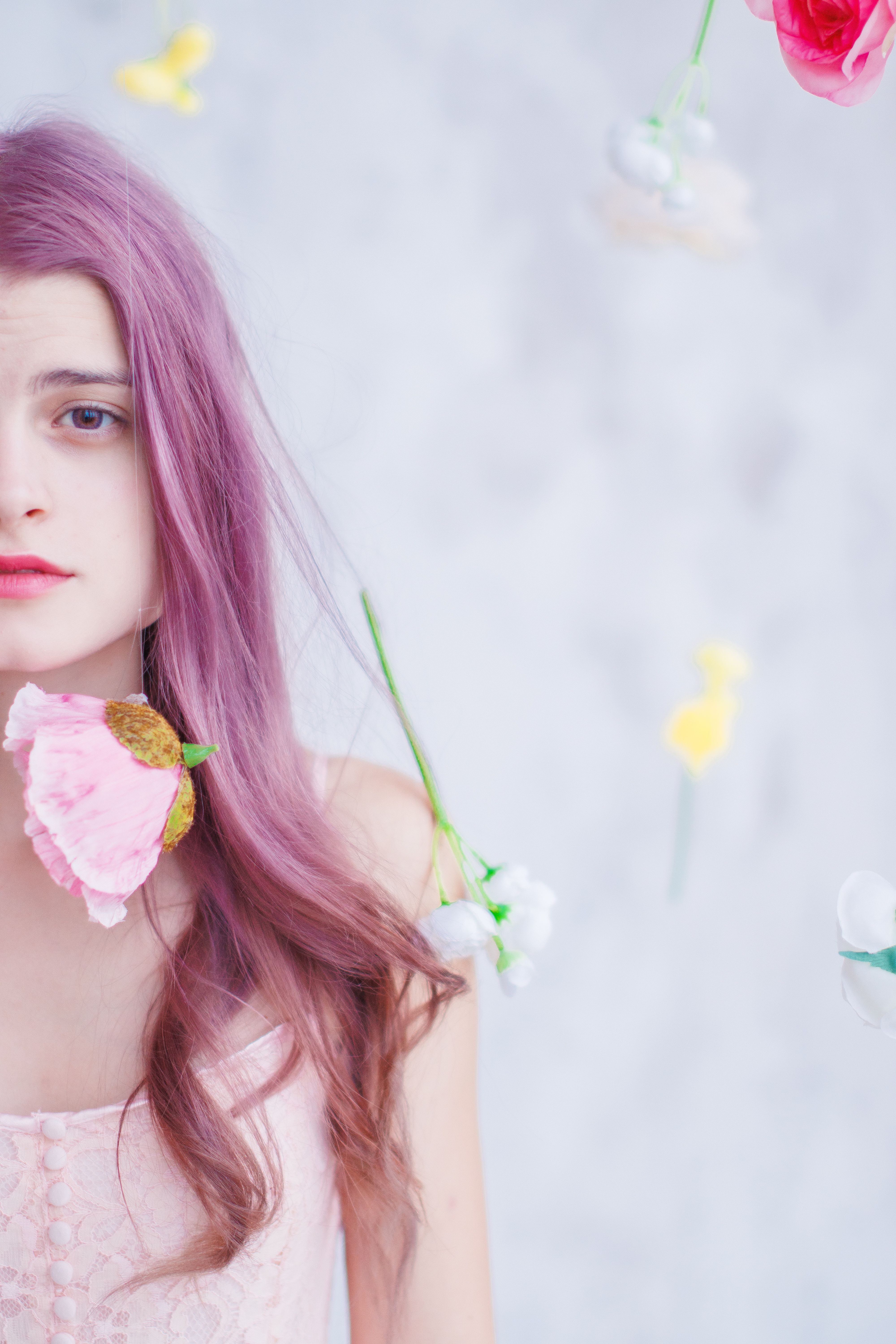 Artistic portrait of a woman with pink hair and floating flowers on a white background.