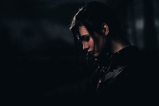 A dramatic portrait of a woman with black hair in a dark setting, evoking mystery and contemplation.