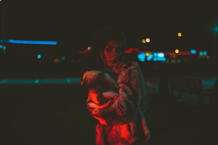 Stylish woman in fur coat under moody red lights at night., by Diogo Cacito on Pexels