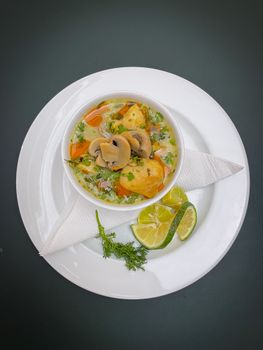 Delicious vegetable soup with mushrooms garnished with lime slices in a bowl.