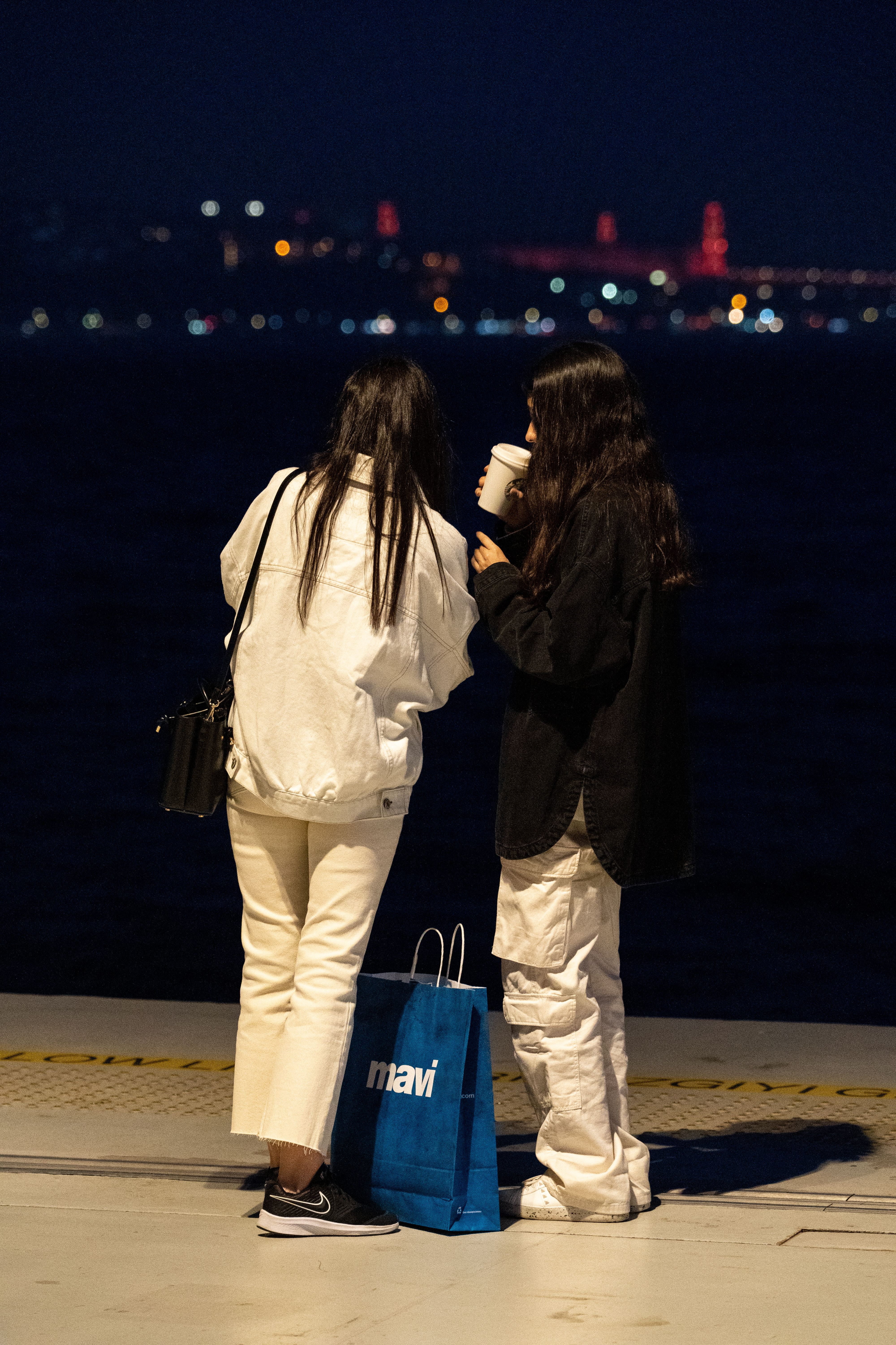 Two women in casual attire enjoying a nighttime cityscape with illuminated skyline in the background.