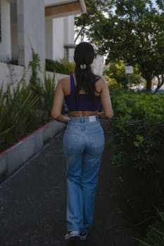 Back view of a woman walking on a verdant city sidewalk during daylight.