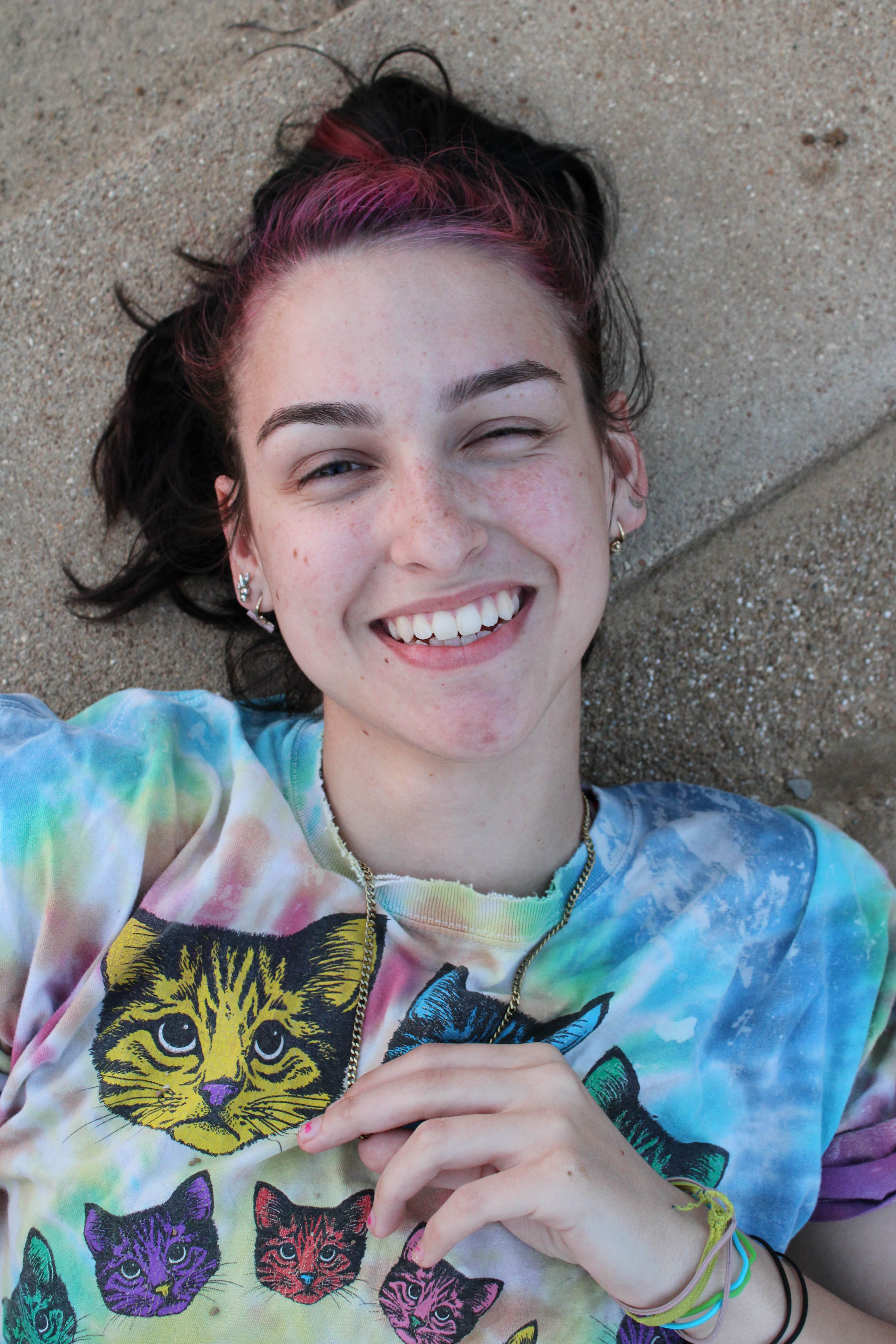 Vibrant portrait of a cheerful woman with dyed hair and a colorful cat-themed shirt.