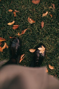 一双黑色的靴子散落在郁郁葱葱的草地上，周围是充满活力的秋叶，捕捉着秋天的神韵