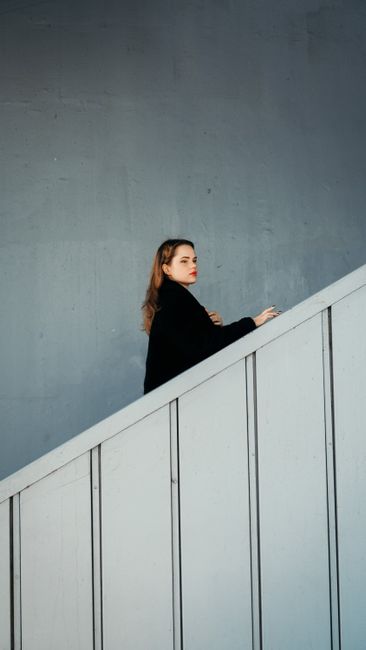 Elegant woman in black coat climbing modern staircase, minimalist architecture