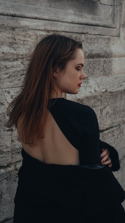 Young Woman in a Black Outfit Standing in front of a Wall 
