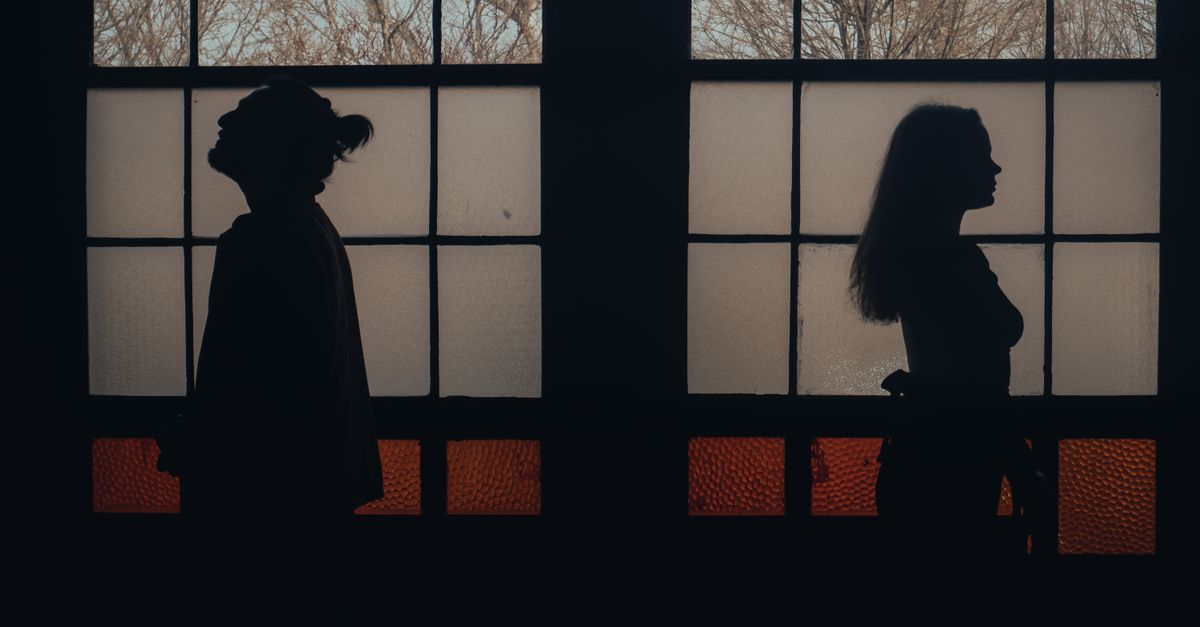 Silhouetted couple standing back to back against a frosted window creates a dramatic silhouette effect.