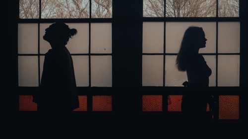 Free Silhouetted couple standing back to back against a frosted window creates a dramatic silhouette effect. Stock Photo