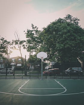 在一个绿树成荫的社区里，一个宁静的篮球场在夕阳下被正面拍摄