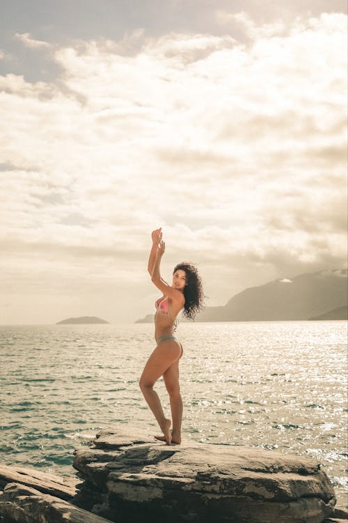 Free Woman in Bikini Standing on the Rock by the Sea Stock Photo