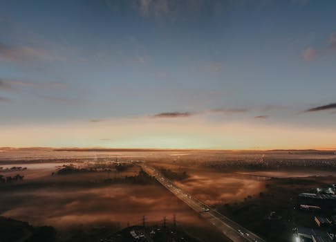 Drone view of a mist-covered road at sunrise in Kealba, Australia, showcasing a tranquil and scenic landscape.