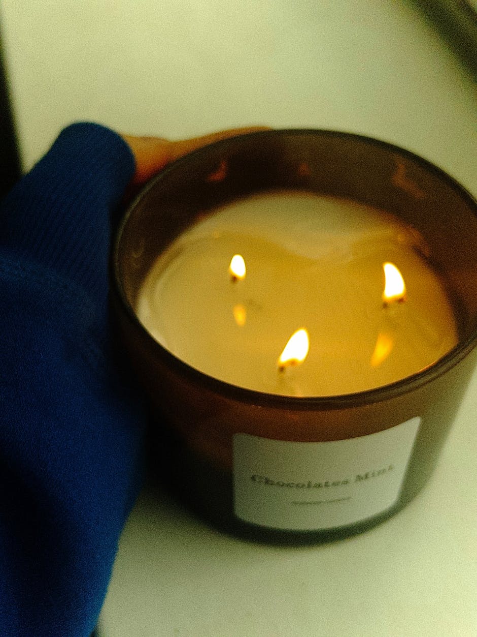 Close-up of a chocolate mint scented candle burning with three gentle flames, held by a person.