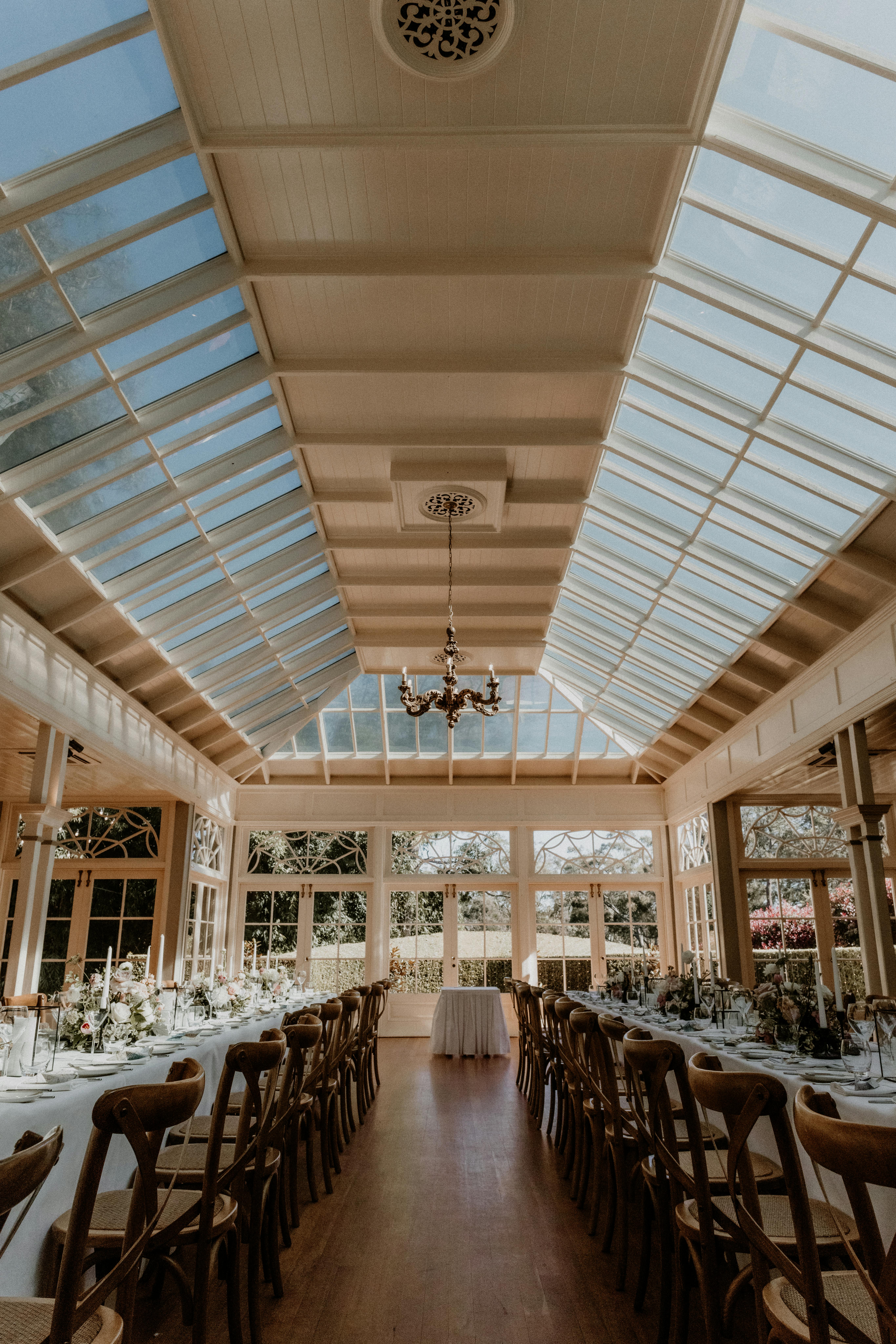 Beautifully arranged wedding reception venue with natural lighting and elegant table settings under a glass roof.