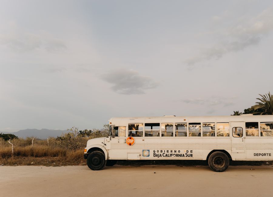 A white school bus parked in the desert landscape of Baja California Sur, Mexico under a clear sky.