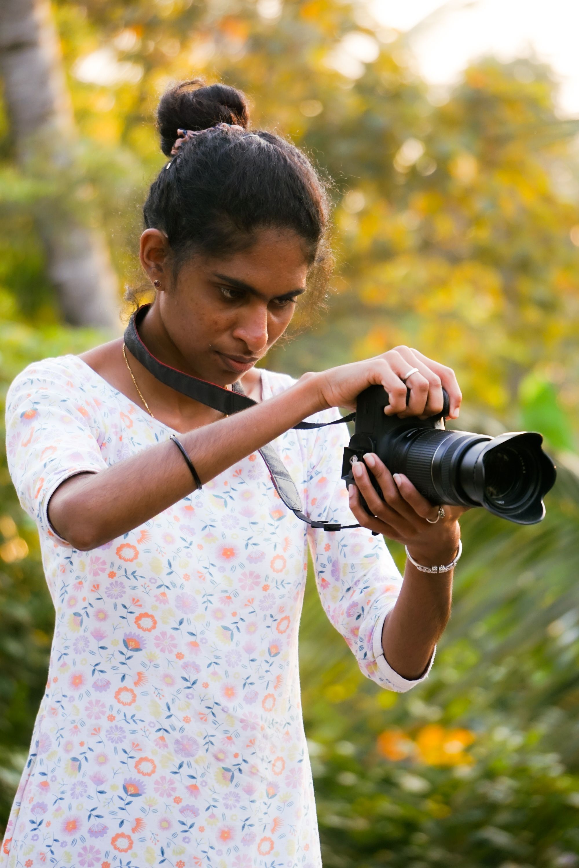 A focused female photographer adjusting her camera in a lush outdoor setting.