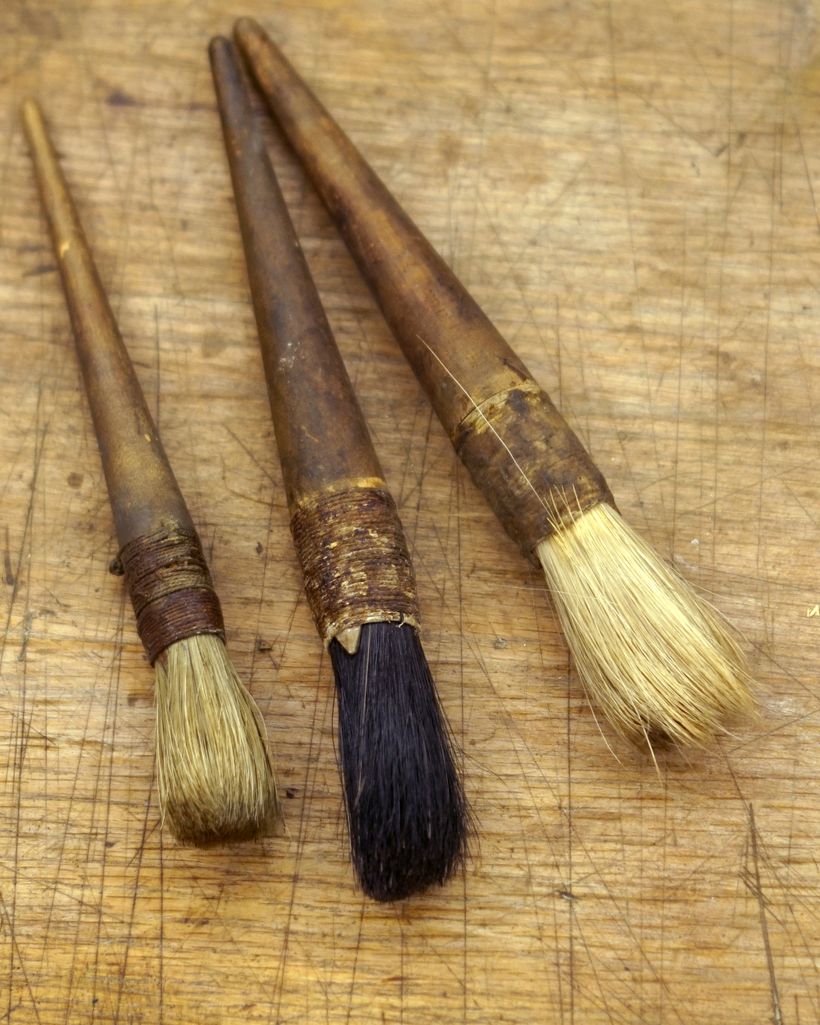 Three worn wooden-handled finishing brushes resting on a scratched workbench — photo by FFD Restorations on Pexels