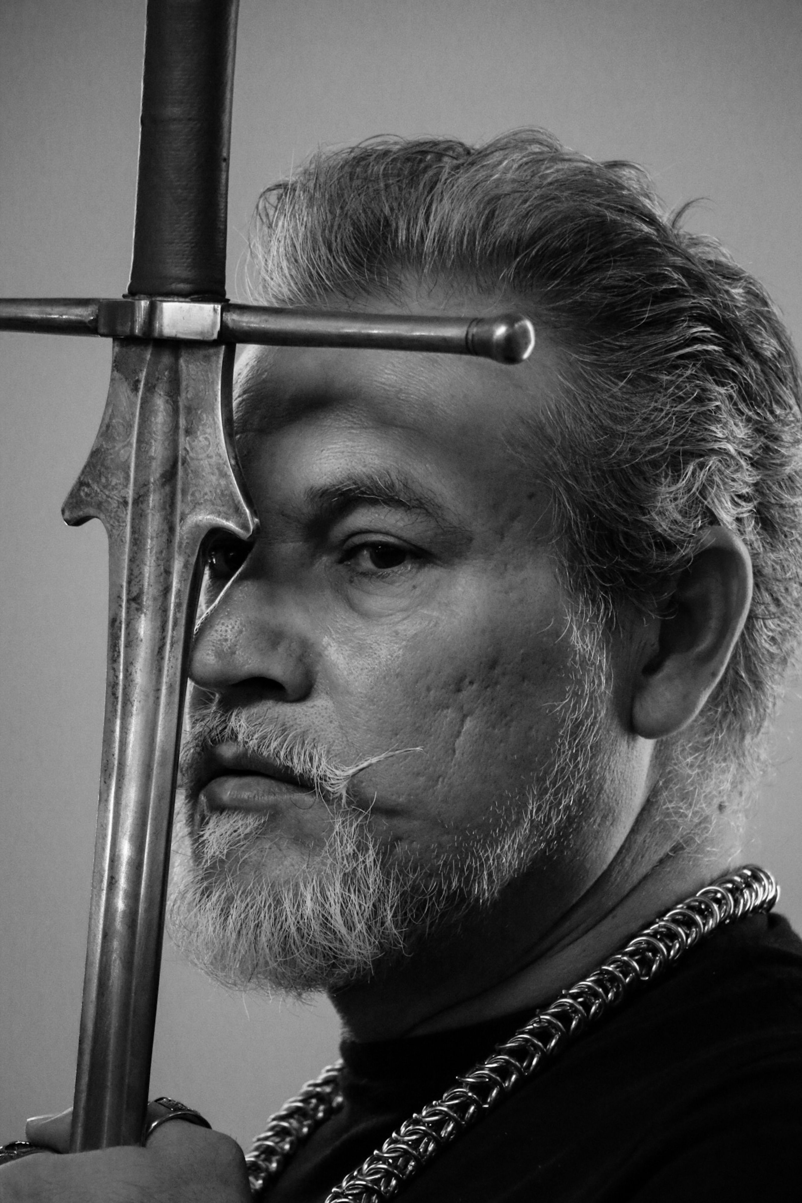 Black and white portrait of a bearded man posing with a sword, evoking mystery.