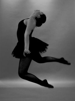 Black and white photo of a ballet dancer performing a dynamic leap in a studio setting.