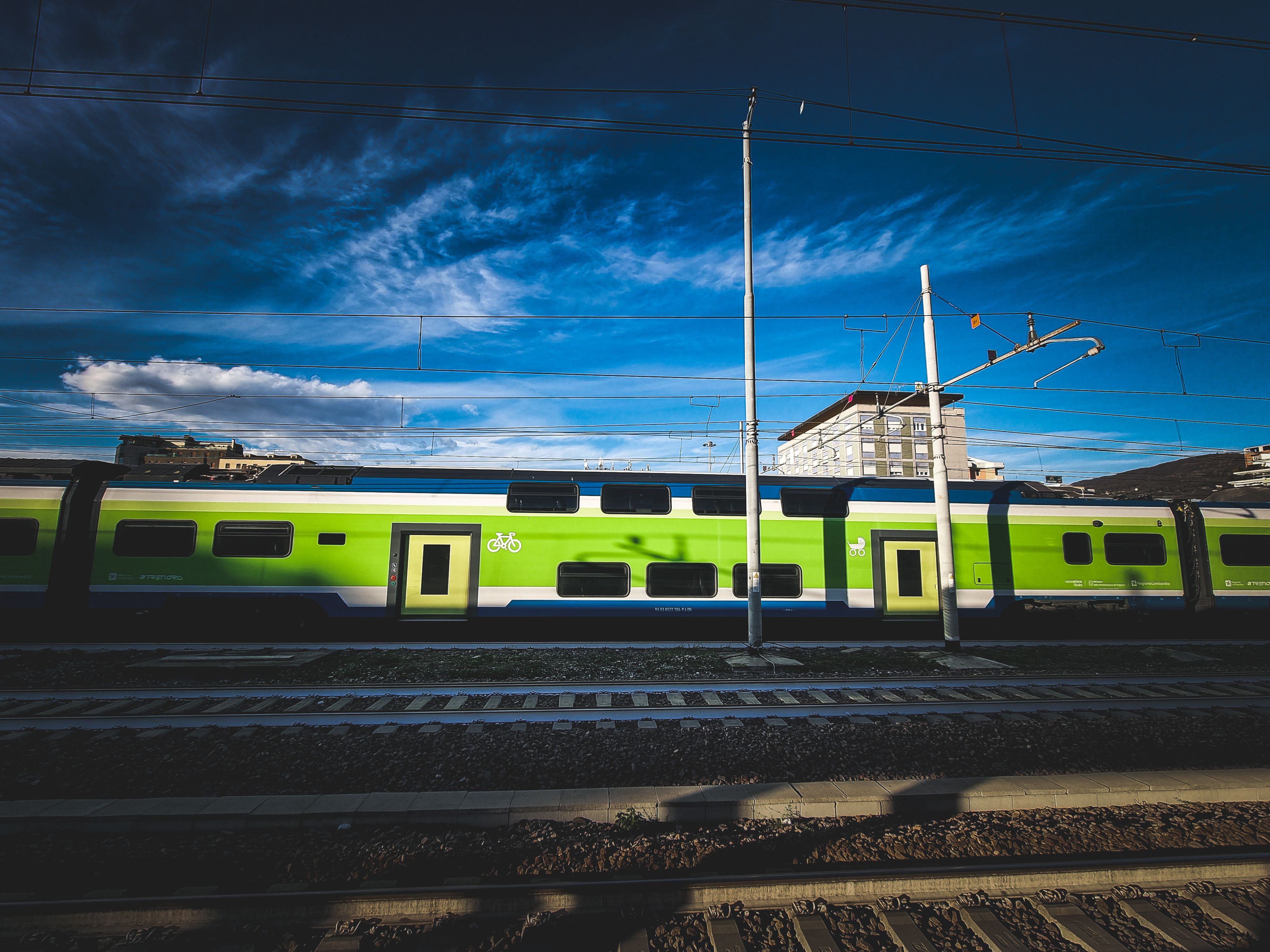 Modern green train at railway station with clear blue sky and urban backdrop.