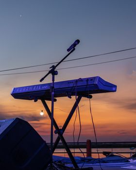 A digital keyboard and microphone set up on an outdoor stage during a vibrant sunset.