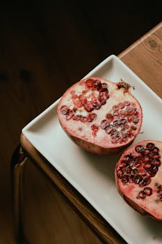 A high angle view of fresh pomegranate halves resting on a white plate, showcasing vibrant red seeds.