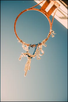 Low angle shot of a rusty basketball hoop with frayed netting under a clear blue sky.
