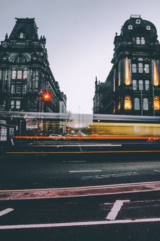 Long exposure capture of evening traffic in an urban area between historic buildings.