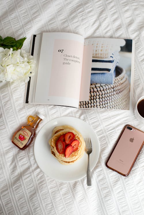 Photo of Breakfast with Strawberry Pancakes and Coffee next to an Open Book and a Smartphone