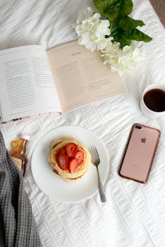 Top view of a cozy breakfast setup with pancakes, strawberries, and coffee on a white background.