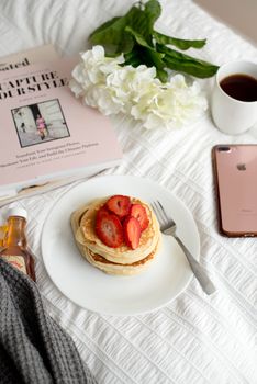 A cozy breakfast with pancakes, coffee, and a book on a white tablecloth.