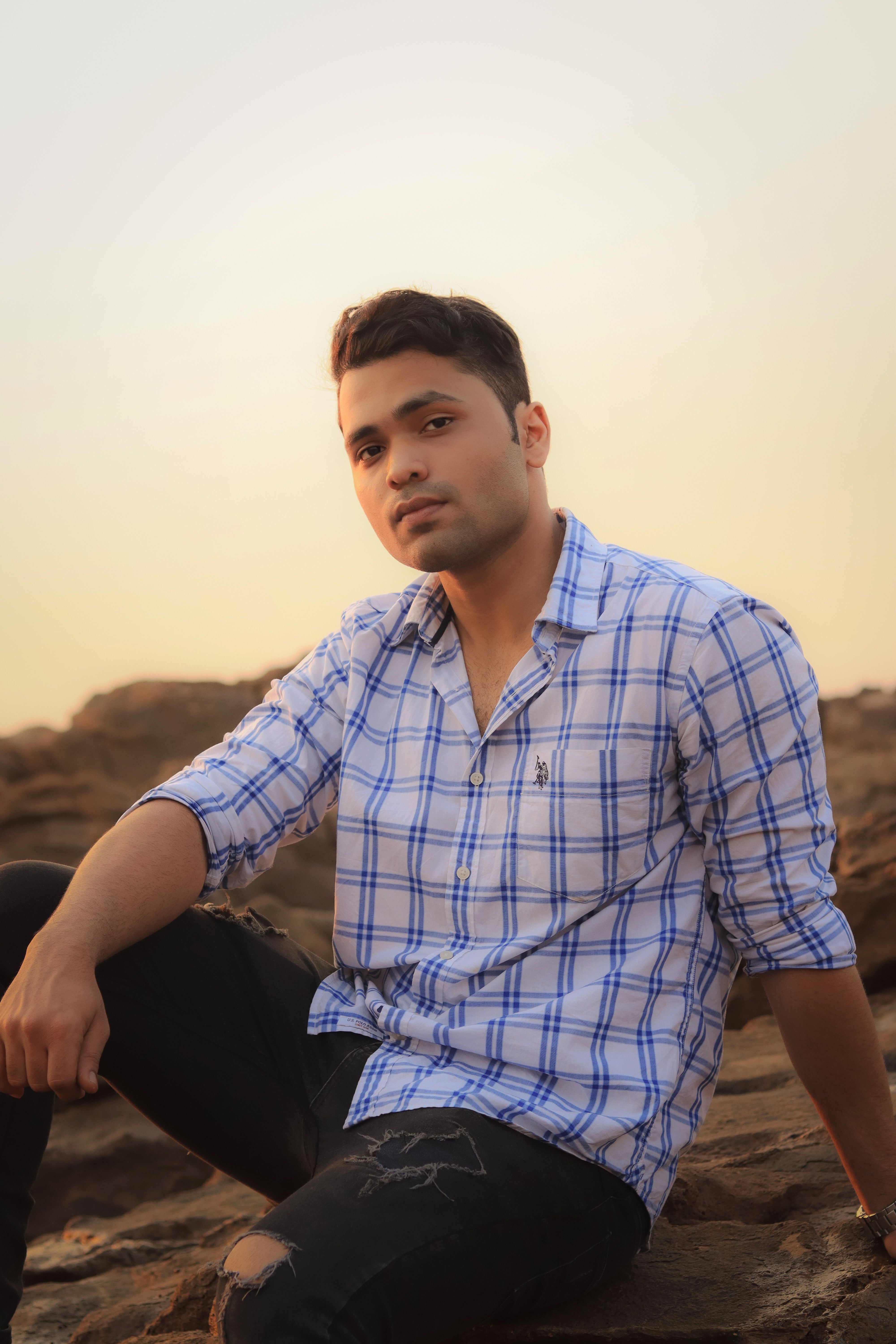 A handsome young man in casual attire posing on rocks during sunset.