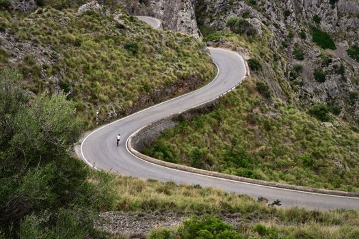A lone cyclist navigates a winding mountain road amidst stunning natural scenery.