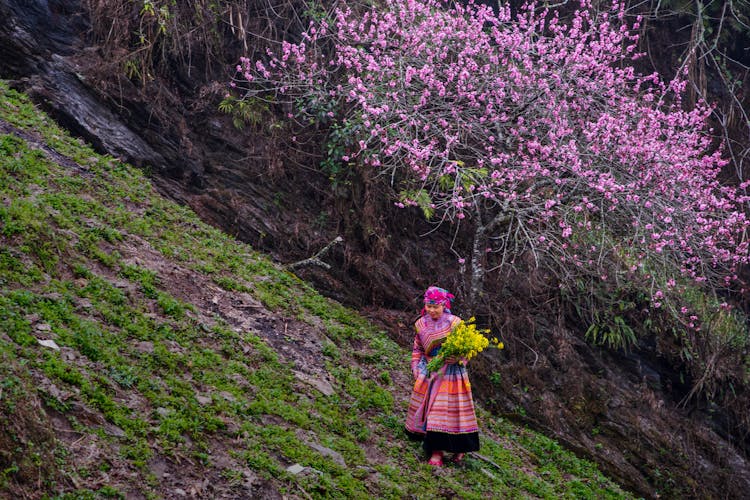 Woman In Traditional Clothing Walking On A Steep Hill With A Bunch Of Flowers