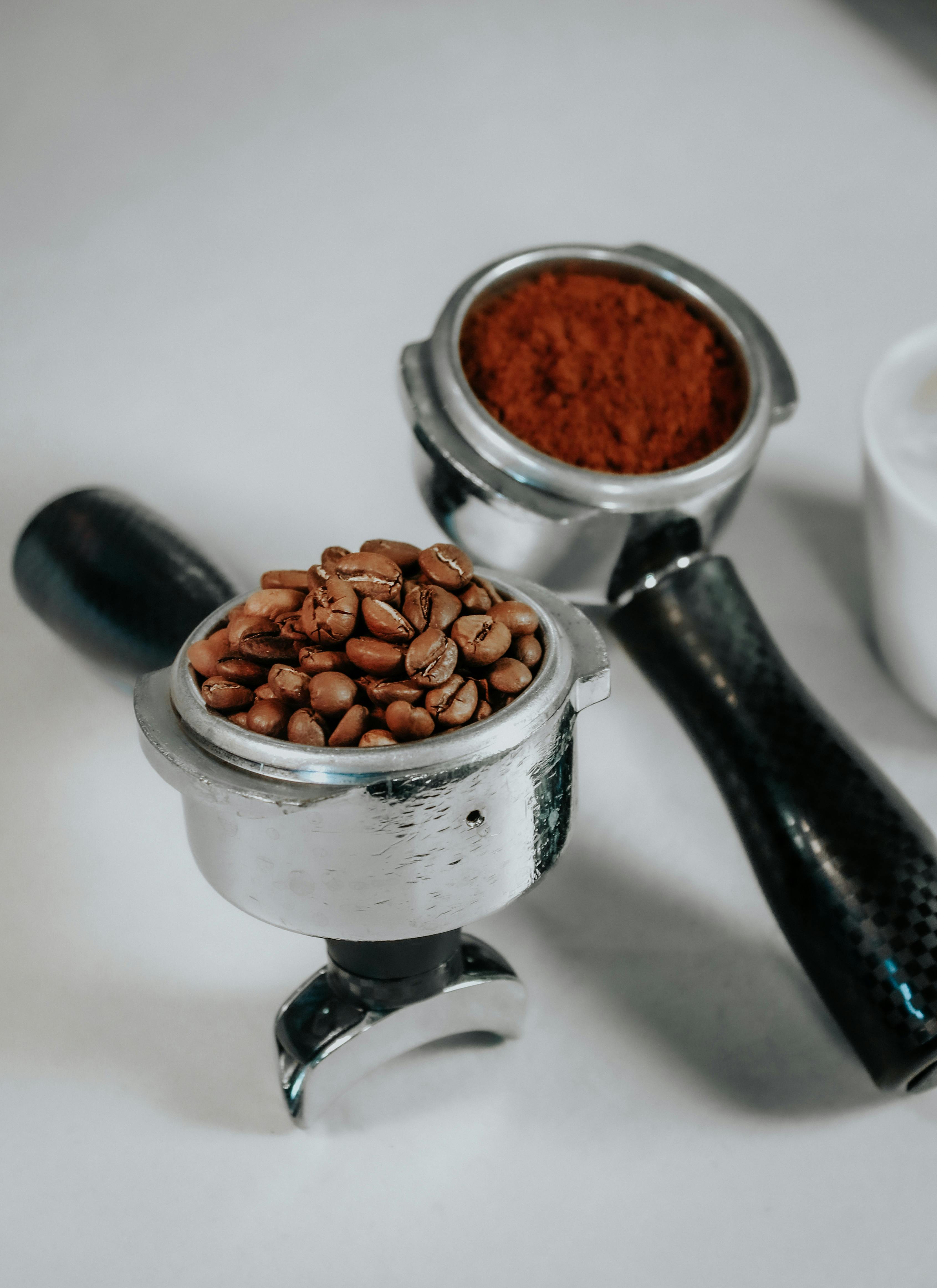 Close-up of espresso portafilters with coffee beans and ground coffee on a white background.