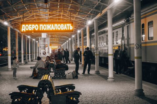 Free Passengers wait at Tashkent railway station under a neon welcome sign. Stock Photo
