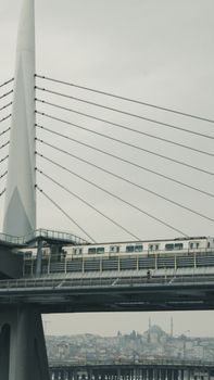 A train crosses a modern suspension bridge in İstanbul, overlooking the cityscape.